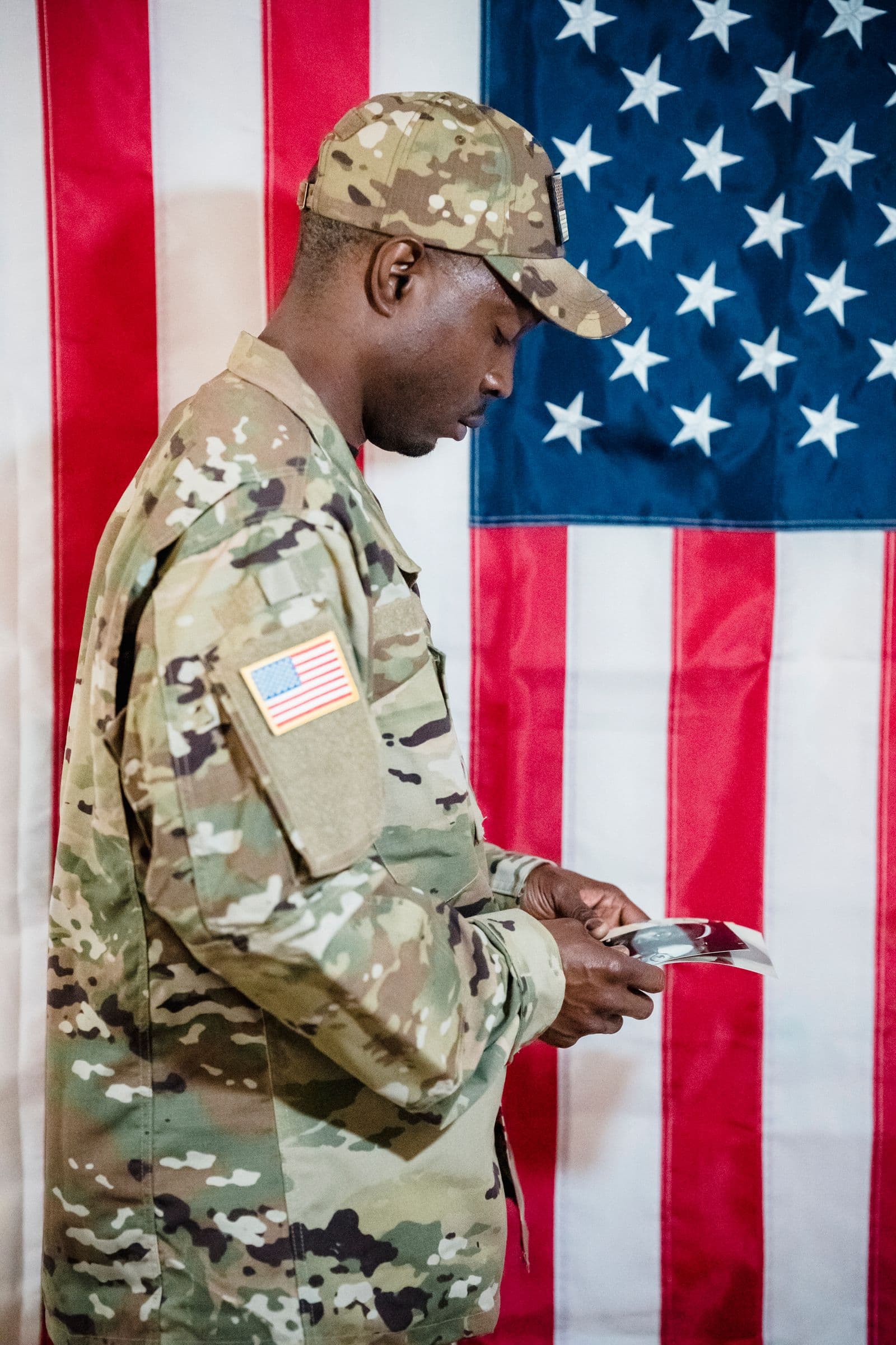 A soldier in uniform stands before the American flag, reading over his paperwork