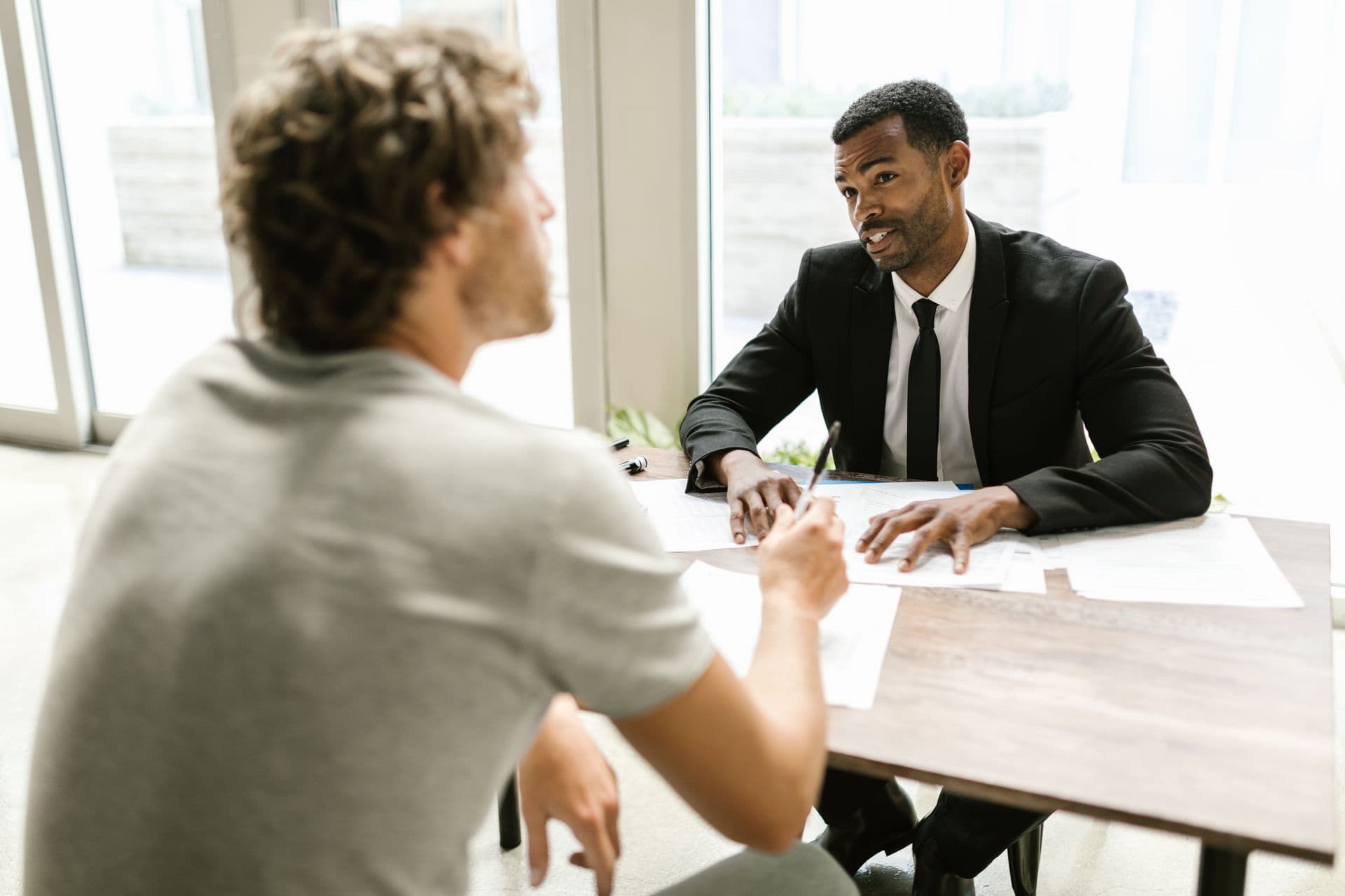 An adviser talks a job seeker through his paperwork across a desk in a sunlit office